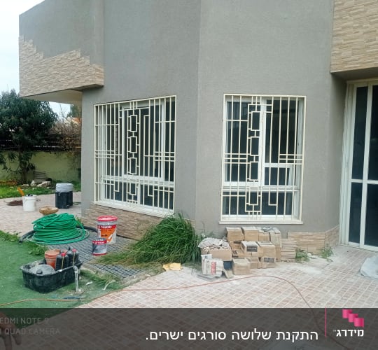 חלונות עם סורגים לבנים על קיר חיצוני אפור